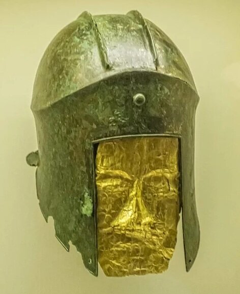  Funerary bronze helmet with gold mask from the necropolis at Archontiko Greek 525-500 BCE. The bronze nail on the front of this helmet would have been used to secure the crest. The small holes on the tips of the cheek guards were used for lacing the